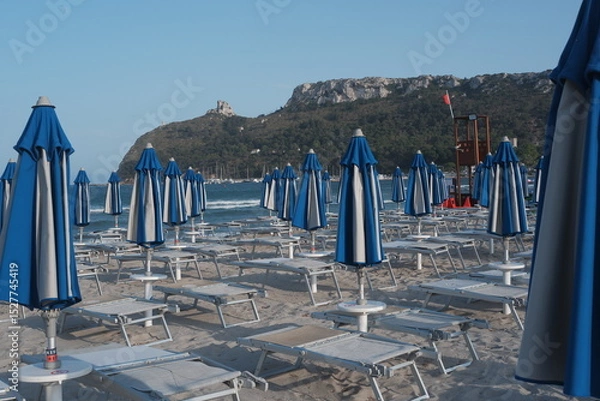 Obraz Closed umbrellas on sandy beach in Sardinia, Poetto shore with summer mood and calm coastal atmosphere