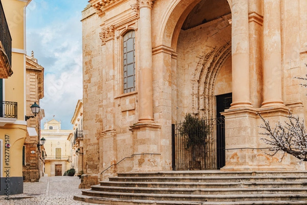 Fototapeta An elegant side entrance of the Ciutadella de Menorca Cathedral, featuring grand columns, an arched doorway, and intricate stone detailing. The blend of styles in Menorca religious landmark