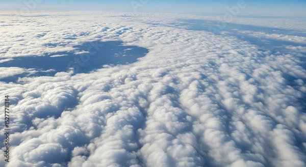 Fototapeta Aerial view of thick, fluffy clouds forming a white blanket with a large circular clear patch under a soft blue sky on the distant horizon.