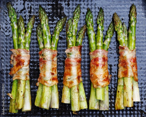 Obraz Grilling green asparagus wrapped in bacon on a dark background, top view