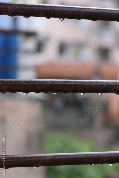 Fototapeta Raindrops clinging to horizontal bars of a railing, blurred city background.