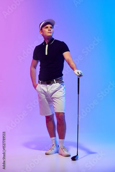 Fototapeta Golf player in dark shirt and white visor finishes confident swing with stable pose and turned shoulders under neon light against gradient background. Concept of golf power, balance, discipline, sport