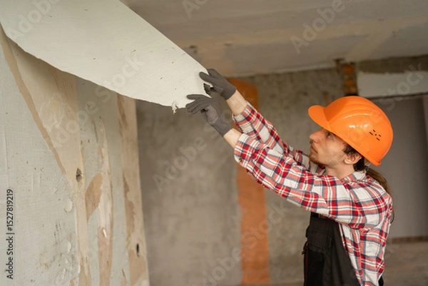 Obraz builder repairman in helmet removing old wallpaper from wall preparing apartment for renovation and interior update