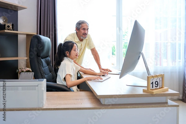 Fototapeta Young asian schoolgirl is doing her class homework assignment at home with advice from grandfather for education and study
