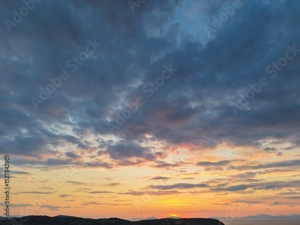Fototapeta Beautiful cloudy red sunrise over sea with beach, waves and mountains in the background. Impressive structure texture in the sky