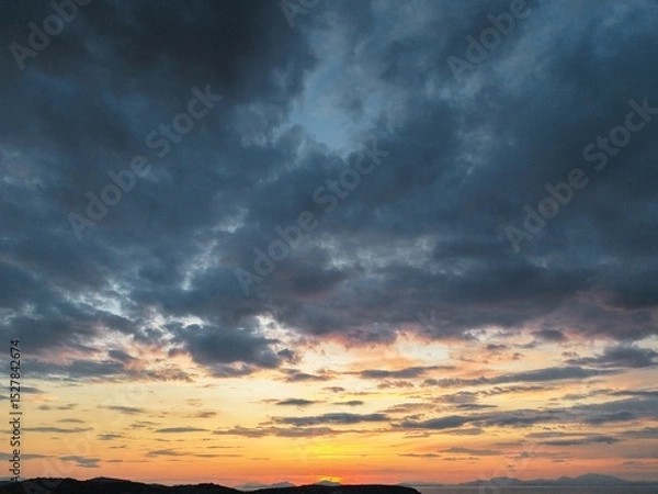 Fototapeta Beautiful cloudy red sunrise over sea with beach, waves and mountains in the background. Impressive structure texture in the sky
