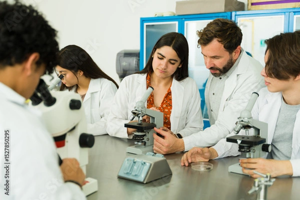 Obraz High school teacher helping students learn biology using microscopes in laboratory