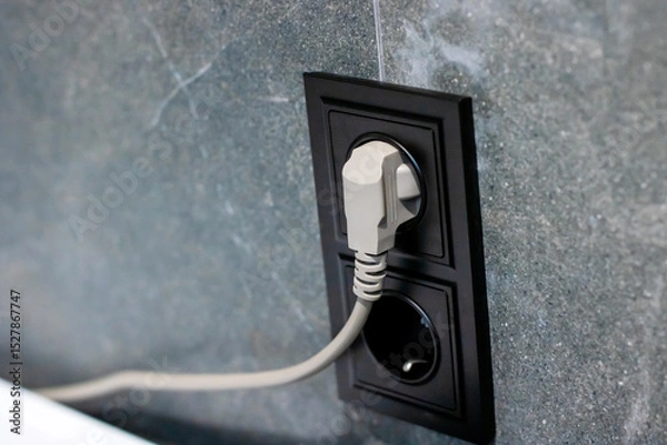 Fototapeta A white electrical cord is securely plugged into a black outlet