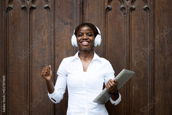 Obraz Portrait of smiling African female student with laptop computer standing by university building door.