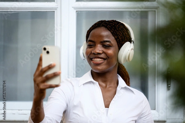 Obraz Positive black girl taking self-portrait photograph while listening to music.