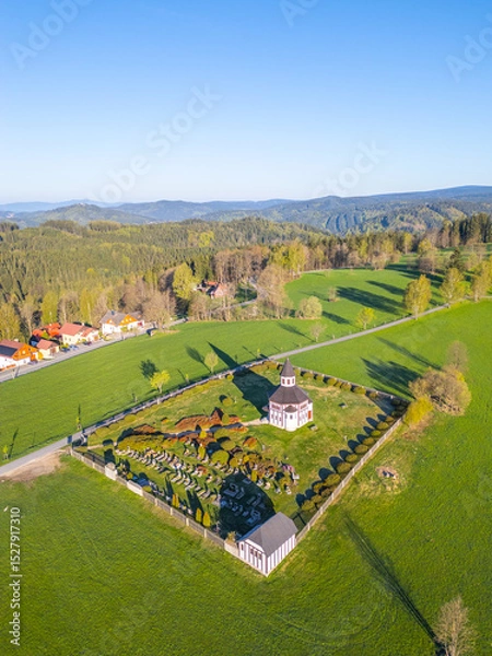 Fototapeta Tesarov Chapel stands majestically in Korenov, surrounded by a serene graveyard and lush green fields. The aerial perspective highlights the natural beauty of the Jizera Mountains.