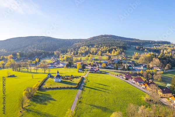 Fototapeta This aerial view captures Tesarov Chapel surrounded by a small graveyard in Korenov, located in the picturesque Jizera Mountains of Czechia. The landscape is lush and inviting during spring.
