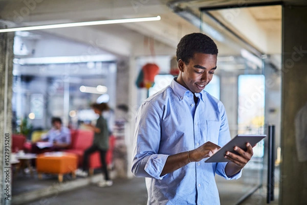Fototapeta Confident young man working on a digital tablet in a modern office setting