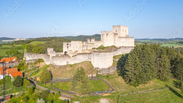 Fototapeta Rabi Castle ruins stand majestically against the backdrop of Czech countryside. This drone view showcases the historical structure surrounded by lush greenery and distant hills on a clear day.