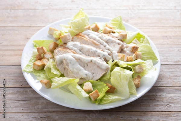 Fototapeta Crunchy Caesar salad with chicken on wooden table