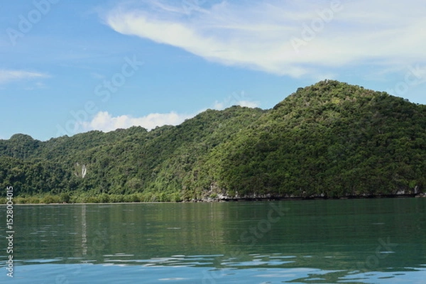 Obraz View of the sky, mountains, and sea during the summer afternoon. The sky is scattered with white clouds. The mountains are covered with green trees, the sea is calm. Natural beauty.
