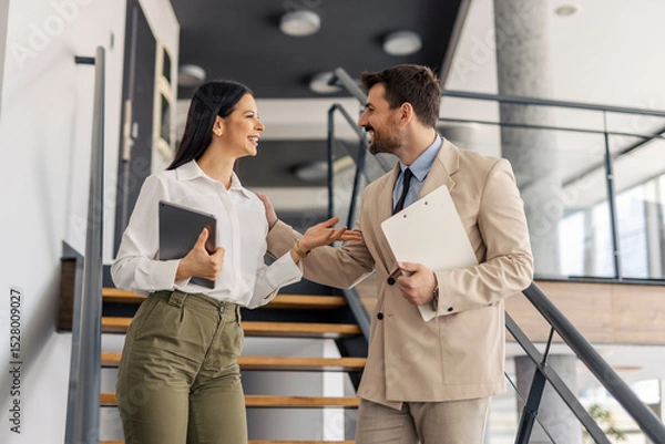 Fototapeta Cheerful elegant businesspeople standing on stairs in minimalistic workspace and discussing.