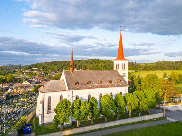 Fototapeta Saint Mary Magdalene Church stands amidst lush greenery in Bohutin, Czechia, showcasing its striking architecture with twin spires. The serene environment invites peaceful reflection.