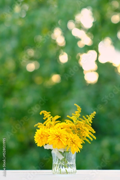 Fototapeta beautiful floral composition with yellow flowers in glass vase on table in garden, natural background. rudbeckia laciniata (rudbeckia golden ball), symbol of summer or autumn season.