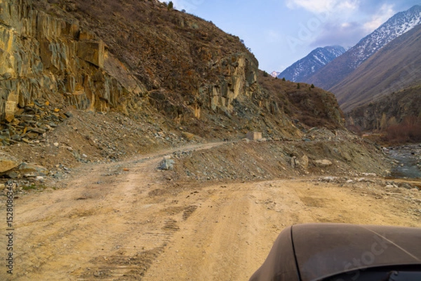 Obraz Dry dirt road winds through a rugged mountainous region, showcasing natural beauty of Kyrgyzstan