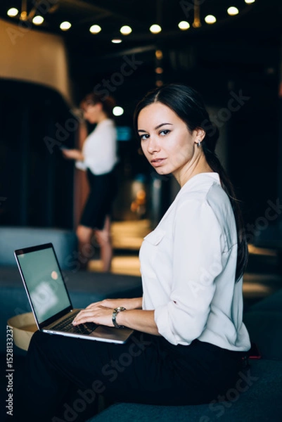 Fototapeta Smart businesswoman in formal wear browsing laptop at lobby of office center