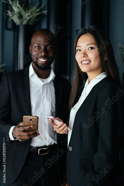 Fototapeta Multiracial confident business people using smartphones before meeting in modern office