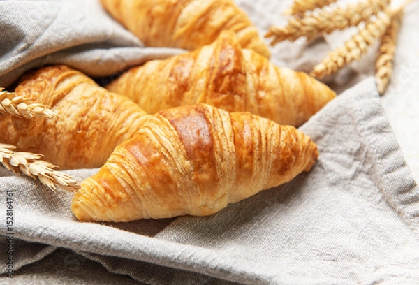 Fototapeta Freshly baked croissants resting on a linen cloth with wheat stalks
