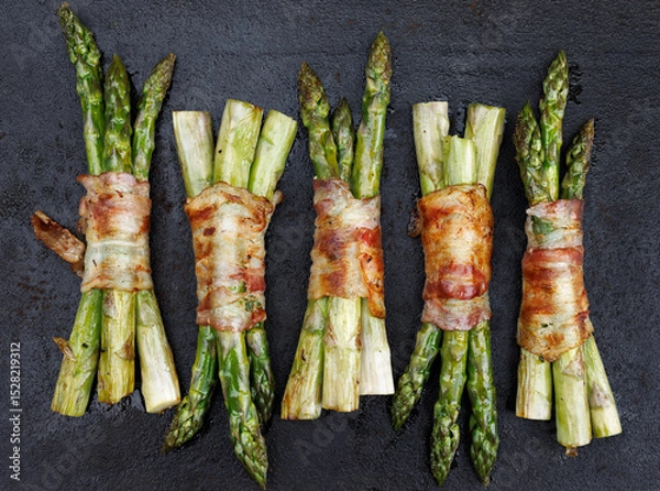 Obraz 
Grilled green asparagus wrapped bacon on a dark background, top view
