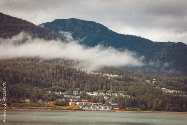 Fototapeta Cruise ship at a port in Juneau, Alaska with snow capped mountain and low lying fog in the background