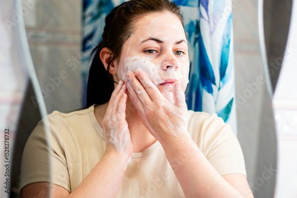 Fototapeta Woman doing facial cleansing ritual with foaming wash. Image for wellness and skincare products. International Self Care Day.