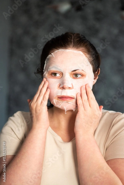 Fototapeta Woman doing skincare ritual with hydrating face mask. Evening beauty routine to soothe facial skin after hard day. Self care concept.