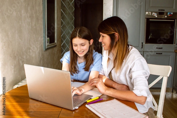 Fototapeta Family digital leisure time. Caucasian mother and daughter using laptop doing online activities, surfing internet, making video call in home interior.