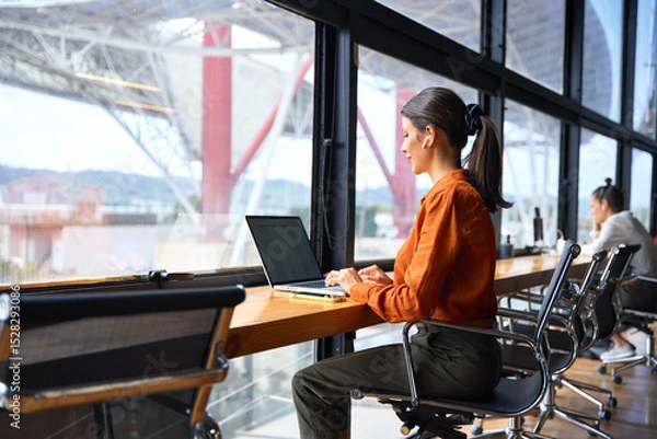 Fototapeta Focused financial specialist latin hispanic businesswoman working on laptop pc sitting at desk in modern office. Middle eastern or european woman using computer for finance data analysing work online