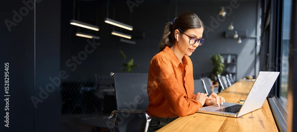 Fototapeta Latin hispanic young business woman working on laptop computer at office desk with city view. Indian entrepreneur manager businesswoman using pc for work, learning at workplace. Banner, copy space