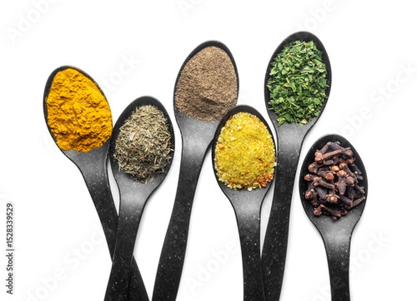 Fototapeta Top view of six black spoons filled with colorful spices and herbs on a white background