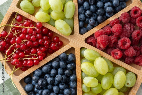 Obraz Top view of colorful fresh berries and grapes served in wooden tray on table. Concept of healthy eating, organic food, summer fruit variety and balanced nutrition for active lifestyle