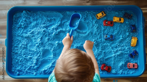 Fototapeta Child Engaging with Blue Kinetic Sand and Toy Cars in Sensory Play Activity. Image made using Generative AI.