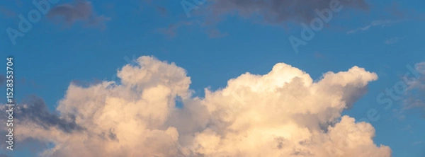 Obraz A cluster of large, sunlit clouds against a blue sky, suggesting impending twilight or dawn