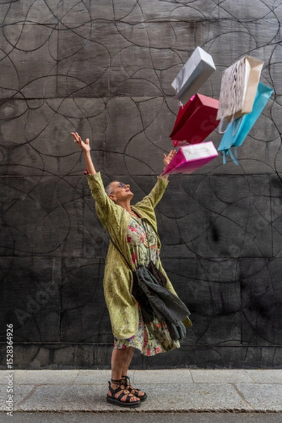 Obraz elegant mature woman having fun throwing colorful shopping bags up in front of a black wall