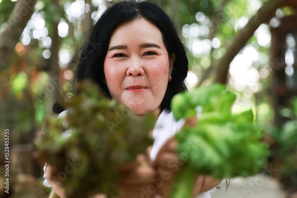 Obraz A joyful plus-size woman smiling warmly while holding fresh leafy greens in both hands,healthy living and natural foods