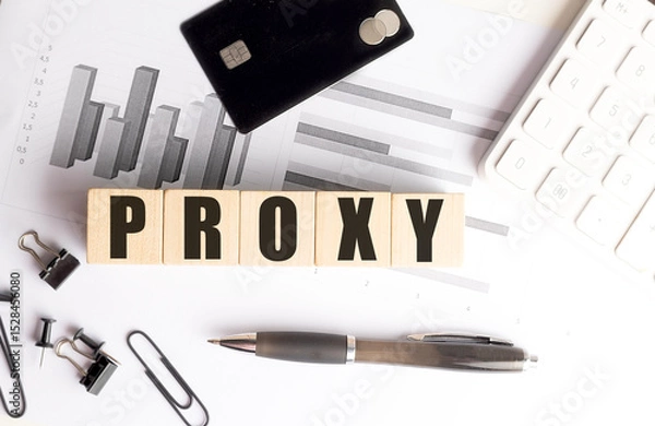 Fototapeta Proxy word on wooden blocks with charts, credit card, pen, clips and calculator on white office desk