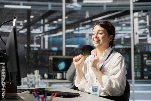 Fototapeta Joyous IT expert in data center office satisfied after checking report showing stable equipment performance. Happy server hub staff member relieved after successfully completing operations.