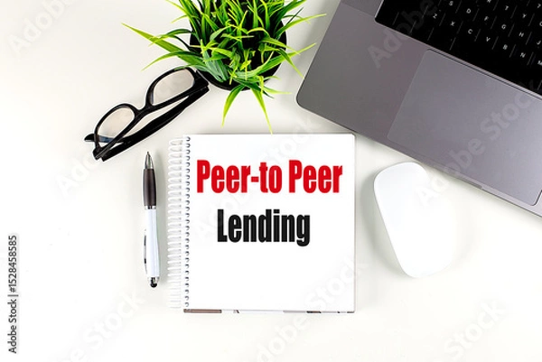 Fototapeta Peer-to-peer lending text on spiral notebook with laptop, glasses, pen, mouse and plant on white desk