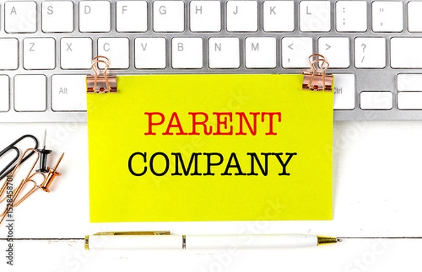 Fototapeta Parent company text on yellow paper sheet pinned on keyboard with pen and office supplies