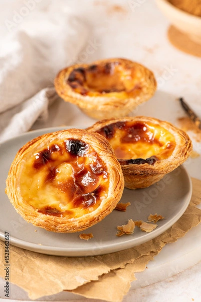Obraz Three Pastel de Nata, Portuguese custard tarts, are presented on a plate with cinnamon and vanilla beans.