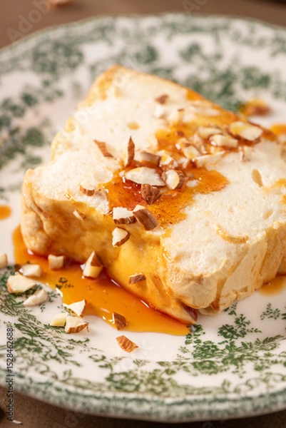 Obraz A close-up showcases a slice of traditional caramelized egg white pudding known as molotof or molotov, generously drizzled with sweet syrup and sprinkled with almond pieces, on a decorative plate