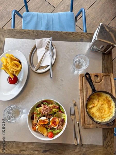 Obraz A vibrant brunch spread featuring a fresh salad, cheesy omelette, and golden fries with ketchup, set in a cozy eatery.