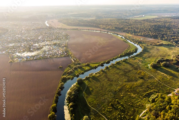 Fototapeta Aerial view of rural landscape with smoke from fires, meandering river going into the distance