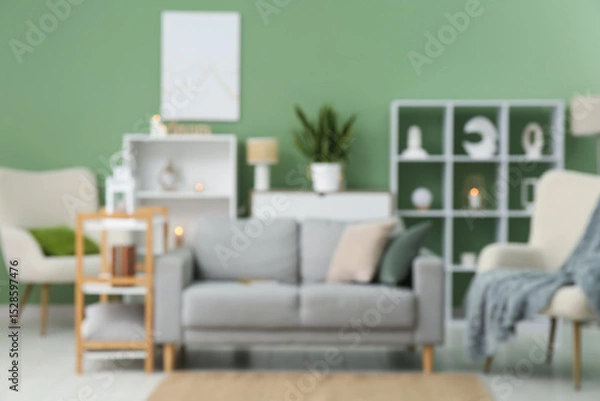 Fototapeta Cozy sofa, armchair and shelving unit in interior of living room. Blurred view