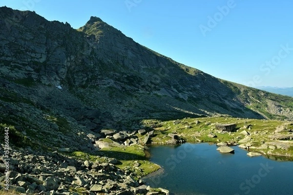 Obraz The shadow of the rising sun from a high cliff barely touches the edge of a beautiful lake in a picturesque mountain valley.